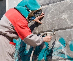 Man removing graffiti from a wall photo leading to graffiti removal and protection products page